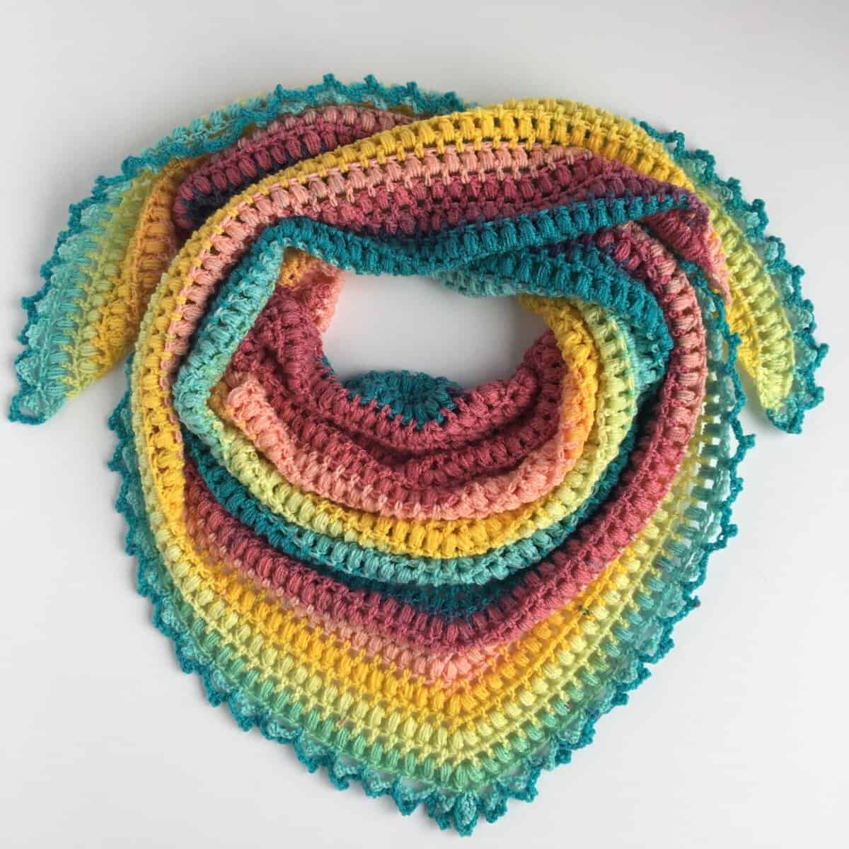 Colorful crochet puff stitch triangle scarf in self-striping yarn, laid flat on white background – free crochet puff st scarf pattern by Nana's Crafty Home