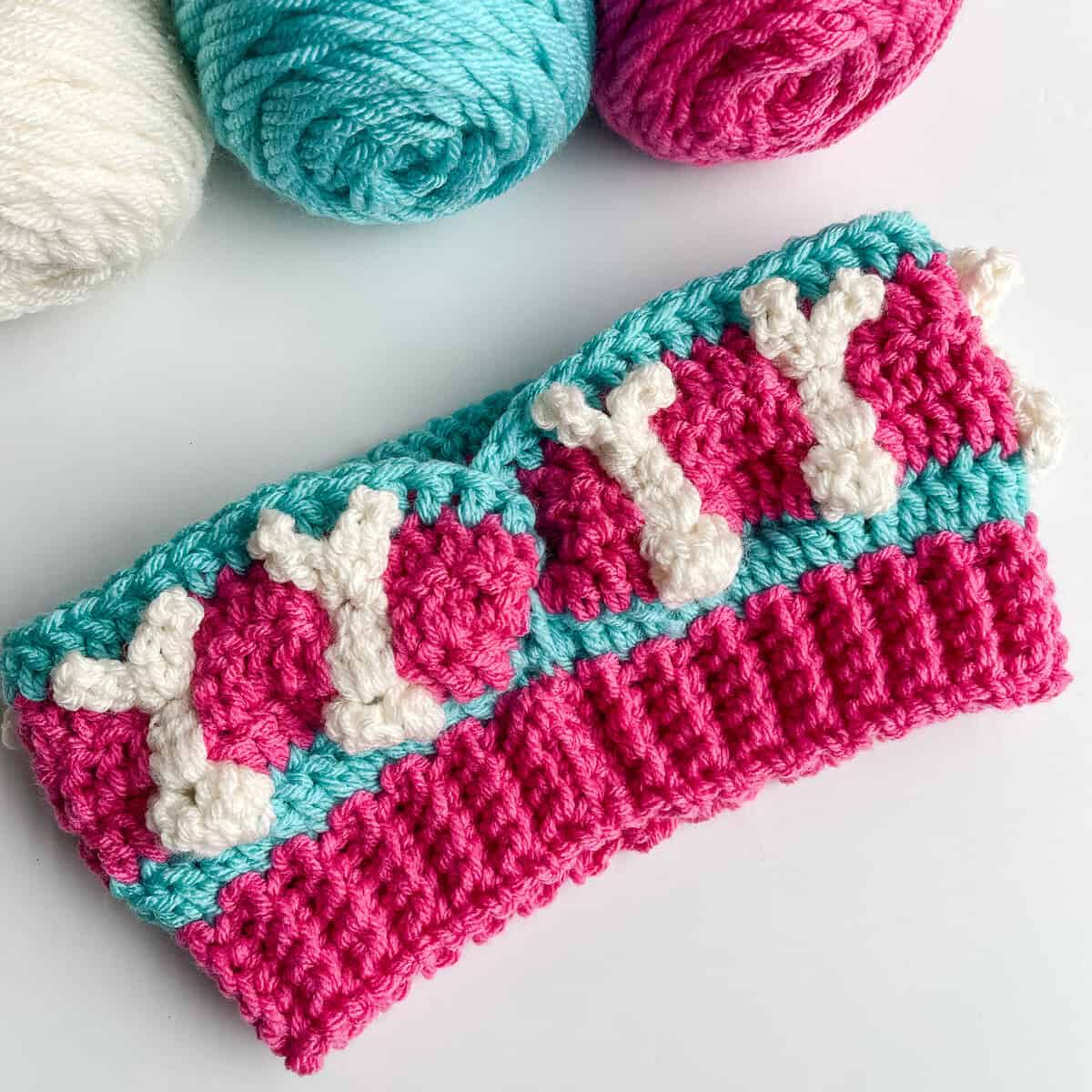 Free crochet bunny headband pattern in hot rose and turquoise with ivory raised bunny bobble stitches, shown as a flat lay with yarn
